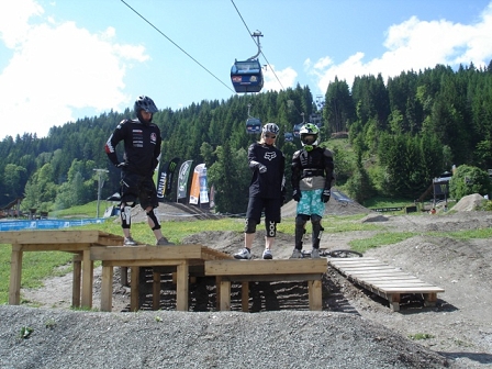 Drei Personen stehen in voller Schutzausrüstung auf Holzrampen und schauen sich die Landung eines Sprunges an.